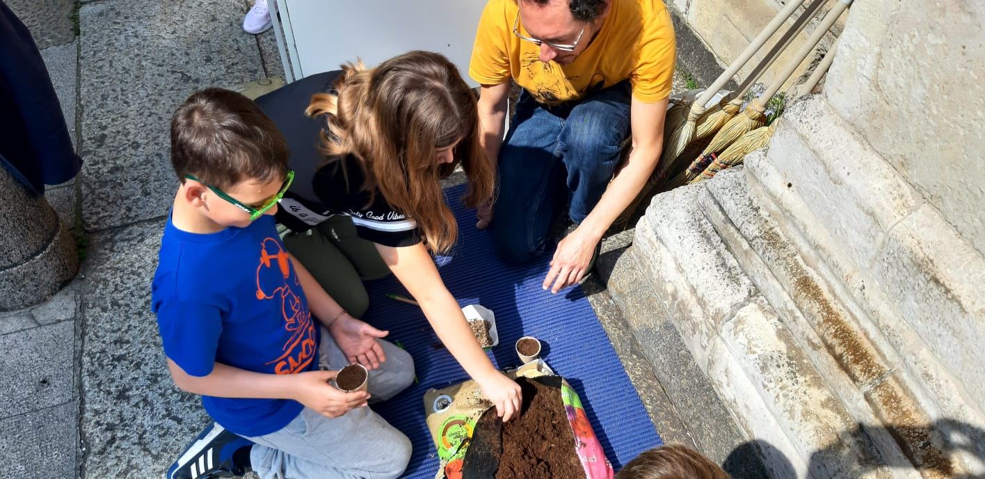 Bambini riempiono vasetti di terriccio insieme a un educatore